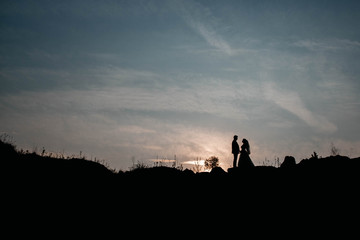 Fototapeta premium Silhouettes of a young couple lovers at sunset on dramatic sky background. Place for text or advertising