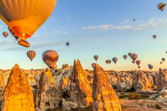 Bright morning as many hot air balloons float in clear skies just above the valleys and homes in Cappadocia