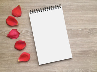 Blank notebook with scarlet red rose petals on the light wooden background, flat lay, top view