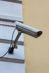 White CCTV security camera on the wall in the city street.