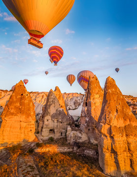 Bright yellow sunrise with colourful balloons floating just above cave homes in Cappodocia