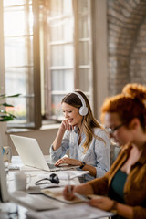 Happy businesswoman with headphones working on laptop in the office.