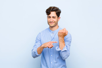 young handsome man looking impatient and angry, pointing at watch, asking for punctuality, wants to...