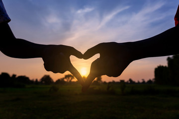 Silhouette hands of two child are symbolized as a heart shape on nature sunset - 300382859