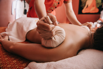 cropped view of masseur doing back massage with herbal balls to woman in spa