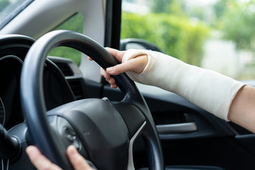 Broken arm woman driving a car. Unsafety driving concept.