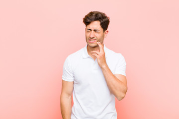 young handsome man holding cheek and suffering painful toothache, feeling ill, miserable and...
