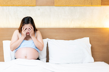 Asian pregnant woman sitting on the bed in unhappy emotion.
