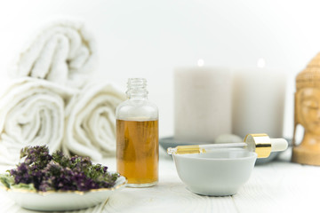 Fototapeta na wymiar Spa treatment bottle of natural organic oil essence serum collagen. Towel, aromatic candles, flowers, massage brush and Buddha on white background. Copy space for text. Beautiful woman hands. Oil drop