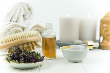 Spa treatment bottle of natural organic oil essence serum collagen. Towel, aromatic candles, flowers, massage brush and Buddha on white background. Copy space for text. Beautiful woman hands. Oil drop
