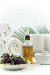 Spa treatment bottle of natural organic oil essence serum collagen. Towel, aromatic candles, flowers, massage brush and Buddha on white background. Copy space for text. Beautiful woman hands. Oil drop
