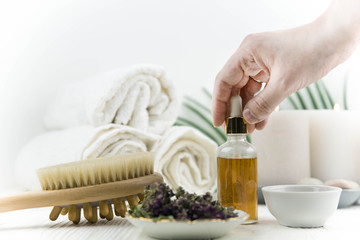 Spa treatment bottle of natural organic oil essence serum collagen. Towel, aromatic candles, flowers, massage brush and Buddha on white background. Copy space for text. Beautiful woman hands. Oil drop