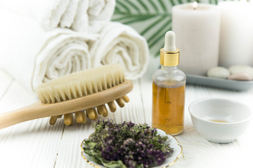 Spa treatment bottle of natural organic oil essence serum collagen. Towel, aromatic candles, flowers, massage brush and Buddha on white background. Copy space for text. Beautiful woman hands. Oil drop