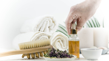 Spa treatment bottle of natural organic oil essence serum collagen. Towel, aromatic candles, flowers, massage brush and Buddha on white background. Copy space for text. Beautiful woman hands. Oil drop
