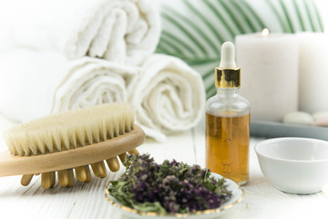 Spa treatment bottle of natural organic oil essence serum collagen. Towel, aromatic candles, flowers, massage brush and Buddha on white background. Copy space for text. Beautiful woman hands. Oil drop