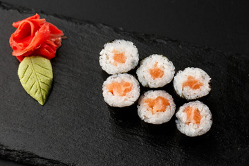 Maki Sushi Rolls with salmon on black stone on dark background. With ginger and wasabi. Sushi menu. Japanese food. Closeup of delicious japanese food with sushi roll. Horizontal photo