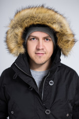 portrait of young handsome man in warm winter jacket over gray background