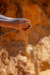 Hands of young boy holding yellow red sand from national park Roussillion, France while dust powder falls through fingers