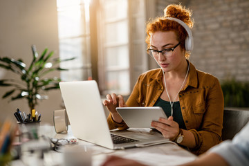 Redhead businesswoman with headphones working on touchpad in the office.