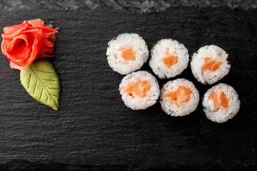 Maki Sushi Rolls with salmon on black stone on dark background. With ginger and wasabi. Sushi menu. Japanese food. Closeup of delicious japanese food with sushi roll. Horizontal photo