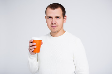 portrait of young man in warm winter sweater drinking coffee over gray background with copy space