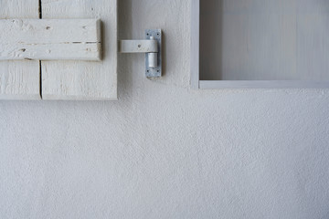 White wall with part of empty shelf and wooden shabby shutter