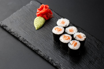 Maki Sushi Rolls with salmon on black stone on dark background. With ginger and wasabi. Sushi menu. Japanese food. Closeup of delicious japanese food with sushi roll. Horizontal photo