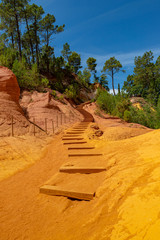 Yellow orange red and ochre sand cover wooden steps in rocky envirement in Roussillion, France,...