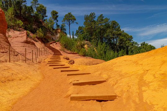 Yellow orange red and ochre sand cover wooden steps in rocky envirement in Roussillion, France, national park in the summer