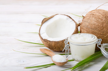 Coconut oil in airtight glass jar spoon and shell pieces on white wooden table