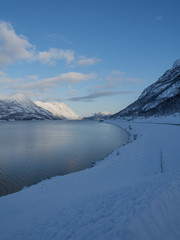 snowy mountains on the shore of the sea with a road and a blue sky in northern Norway in winter