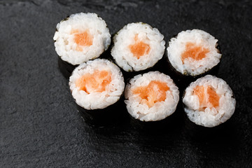 Maki Sushi Rolls with salmon on black stone on dark background. Sushi menu. Japanese food. Closeup of delicious japanese food with sushi roll. Horizontal photo