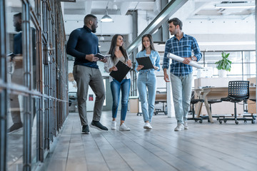 On the way to business meeting. Full length of young modern people in smart casual wear having a discussion while walking through the office