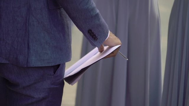 Businessman in blue suit holding folder with paper or documents in hands.