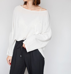 Young woman wearing stylish outfit with a white oversized shirt and black high-waisted trousers isolated on light grey background. Copy space
