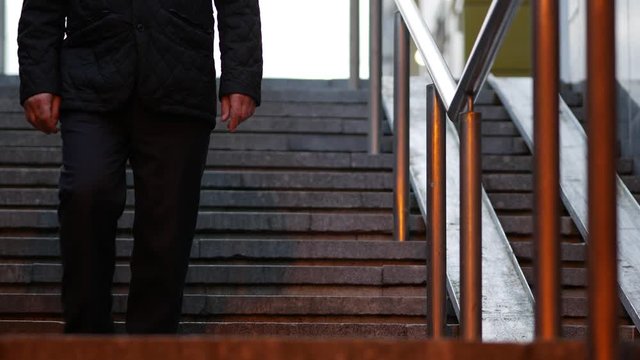 A man goes down the stairs to the underpass. View from the bottom and front. Dusk. Steel railings and stone steps