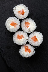 Maki Sushi Rolls with salmon on black stone on dark background. Sushi menu. Japanese food. Closeup of delicious japanese food with sushi roll. Vertical photo