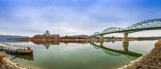 Esztergom, Hungary - Panoramic view of the beautiful Maria Valeria Bridge and Basilica of the Blessed Virgin Mary at Esztergom on an autumn morning. Old mooring ship and reflections on River Danube