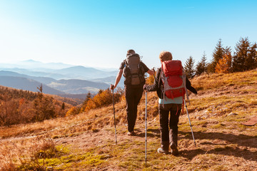 Two old people with large backpacks hike through the autumn mountains, the concept of active...