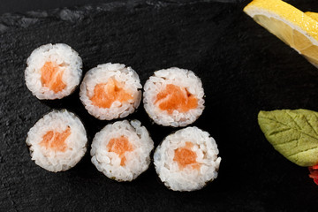 Maki Sushi Rolls with salmon on black stone on dark background. With ginger and wasabi. Sushi menu. Japanese food. Closeup of delicious japanese food with sushi roll. Horizontal photo
