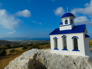 Fototapeta na wymiar Small orthodox church on a white and blue stone with the background of the landscape and the sea