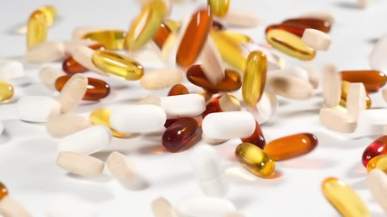 Vitamins and supplements fall onto a white surface in slow motion - Powered by Adobe