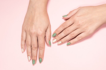 Closeup top view of beautiful two faded colors trendy manicure of green and pink nails with glossy silver stamp design isolated on pastel pink background. Winter or autumn style of nail design concept