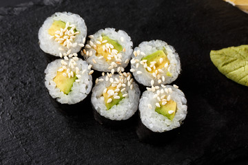 Maki Sushi Rolls with cucumber or avocado on black stone on dark background. Sushi menu. Japanese food. Closeup of delicious japanese food with sushi roll. Horizontal photo