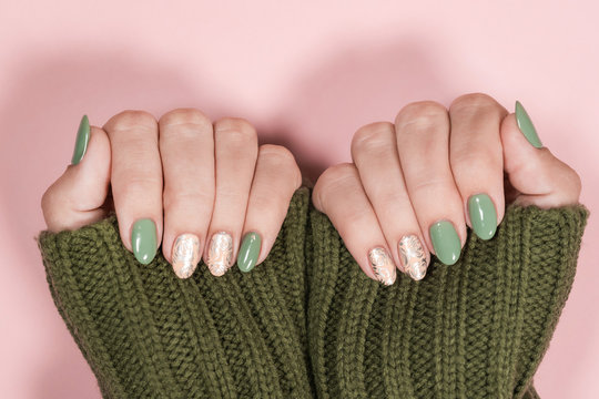Closeup top view of beautiful two faded colors trendy manicure of  green, pink nails with glossy silver stamping design isolated on pastel pink background. Winter, autumn style of nail design concept.