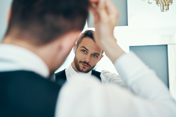 Handsome young man touching his hair with hand standing in front of the mirror