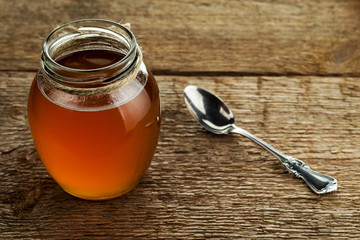 Round glass jar with freshly prepared ghee butter and spoon on wooden background texture..