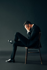 Sad unhappy man in black suit sitting on the chair and closed face by two hands