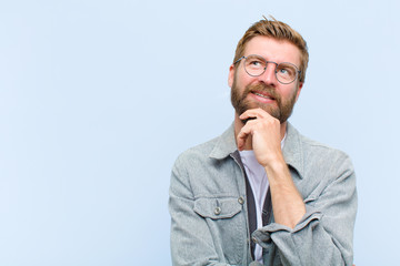 young blonde adult man feeling thoughtful, wondering or imagining ideas, daydreaming and looking up...