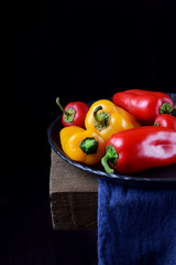 Little red and yellow bell peppers on the wooden table against the black background